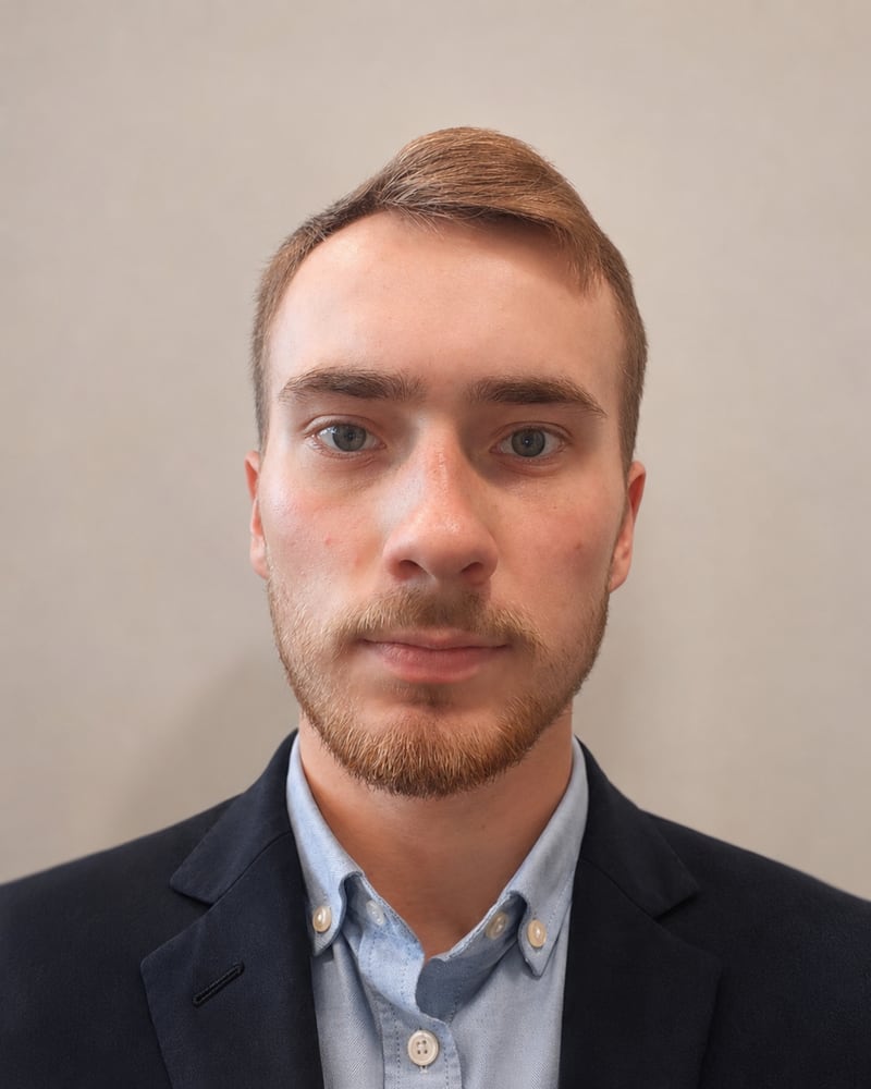 Pavels Kozemjakins, head and shoulders, in a navy jacket and light blue shirt against a plain wall.